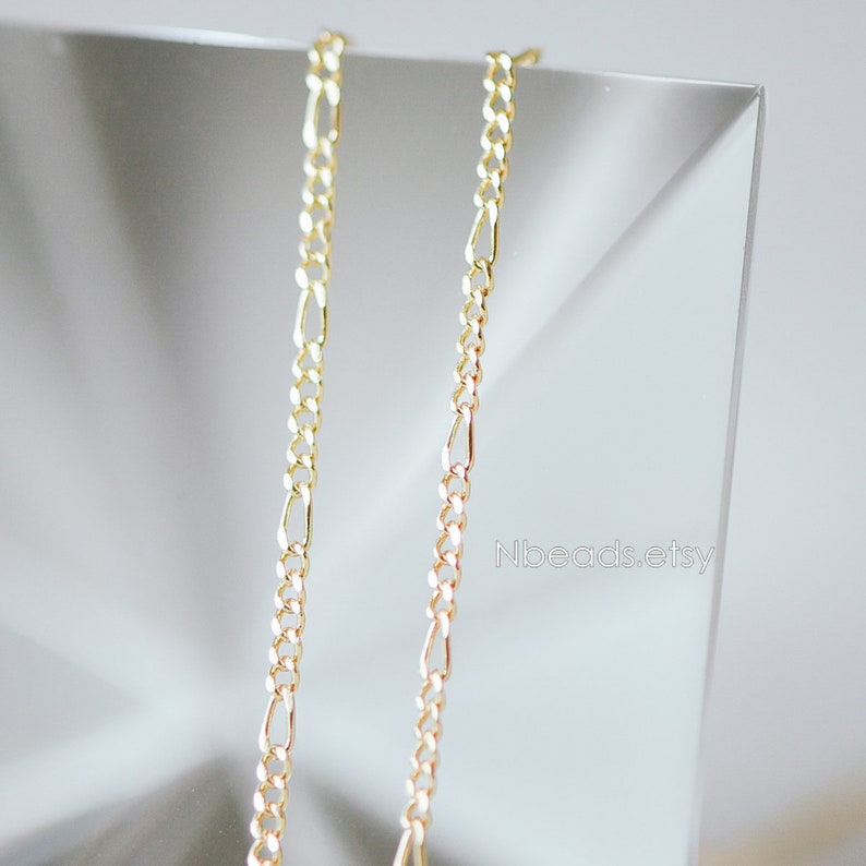 May include: Two gold chains, one slightly longer than the other, are displayed against a white background. The chains are made of a delicate, linked design.