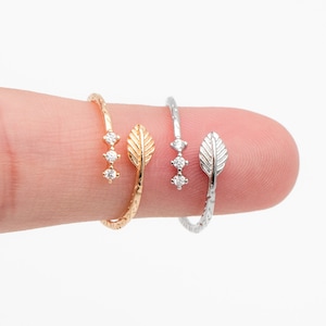 May include: Two delicate rings with a leaf design and three small clear stones. The rings are gold and silver.