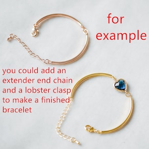 May include: Two gold bracelets, one with a blue heart charm and the other with a chain extender. The text "for example" is written in red above the bracelets.