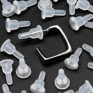 May include: A silver square earring with a post and a variety of clear silicone earring backs.