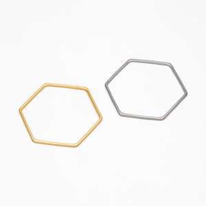 Puede incluir: Dos pulseras de metal en forma de hexágono, una dorada y otra plateada.