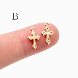 Pu&ograve; includere: Due piccoli ciondoli a forma di croce dorata con un design decorativo. Una croce ha una piccola gemma trasparente in basso. I ciondoli hanno un anello nella parte superiore per il fissaggio ai gioielli. La lettera "B" &egrave; nell'angolo in alto a sinistra.