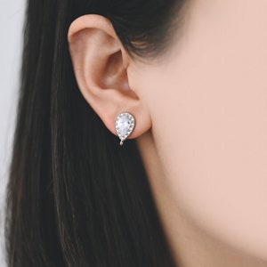 May include: A pair of silver teardrop earrings with a clear crystal stone in the center and smaller crystals around the edge.
