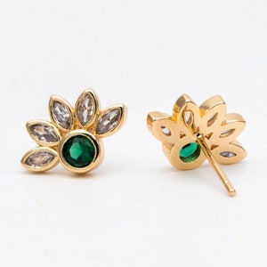 Pode incluir: Um par de brincos de ouro com uma pedra preciosa verde cercada por strass transparentes. Os brincos têm a forma de uma flor com várias pétalas.