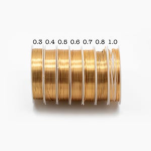 May include: Seven spools of gold wire, each with a different diameter, labeled 0.3, 0.4, 0.5, 0.6, 0.7, 0.8, and 1.0.
