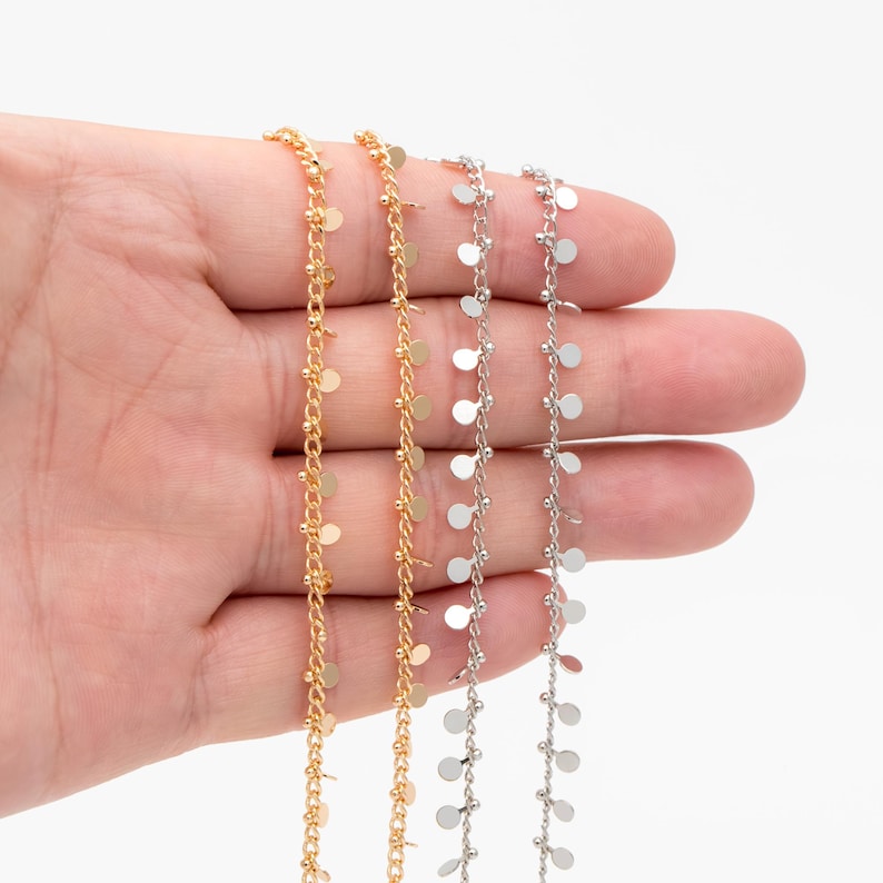 May include: Three strands of chain with small, round, dangling charms. The chains are gold, silver, and silver. The charms are evenly spaced along the chains.