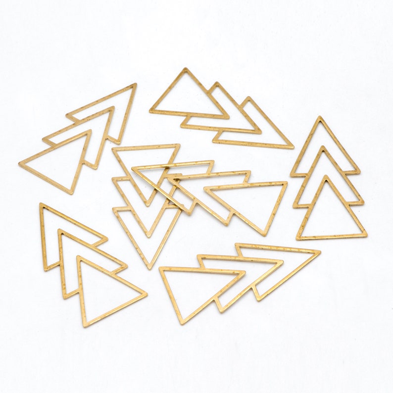 May include: A collection of gold-colored triangle-shaped jewelry findings. The findings are open-framed and arranged on a white surface. The triangles are of varying sizes and are suitable for jewelry making and crafting projects.