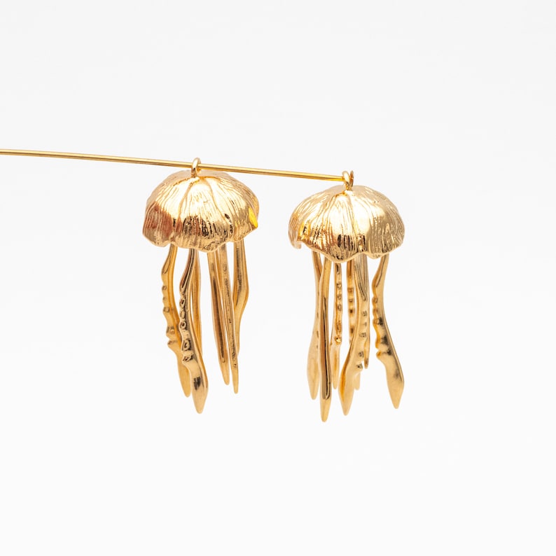 May include: A pair of gold-tone earrings shaped like jellyfish. The earrings have a detailed design with a dome-shaped top and dangling tentacles.