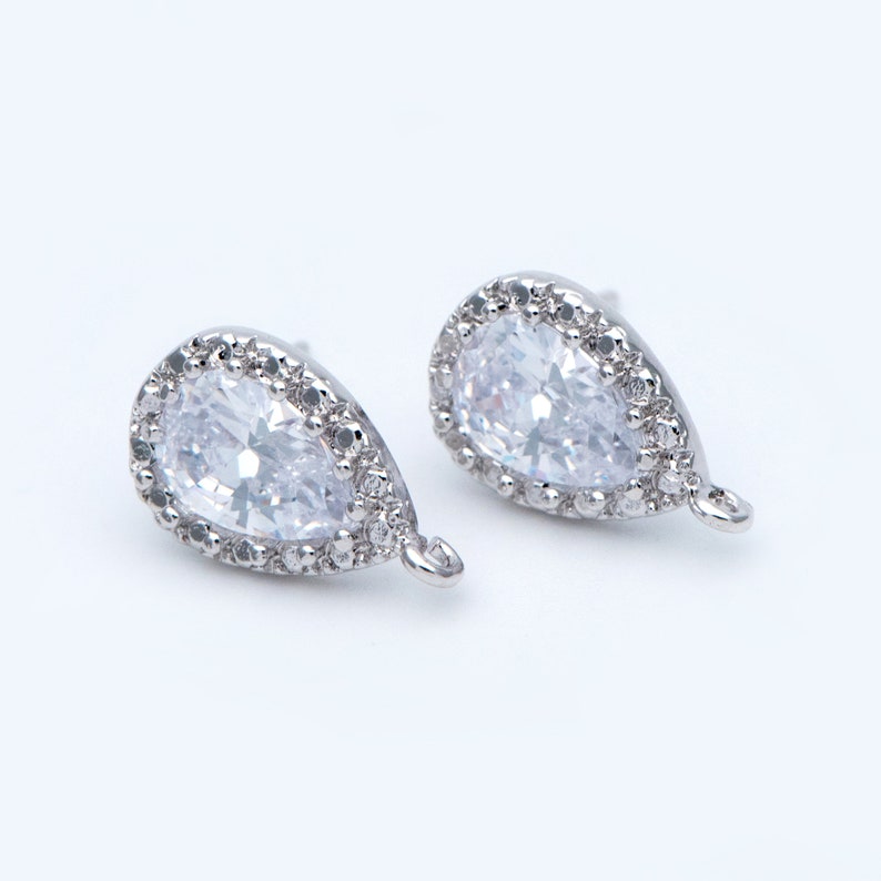 May include: A pair of silver teardrop earrings with clear cubic zirconia stones. The stones are set in a halo of smaller stones and the earrings have a small loop for attaching to a necklace or bracelet.