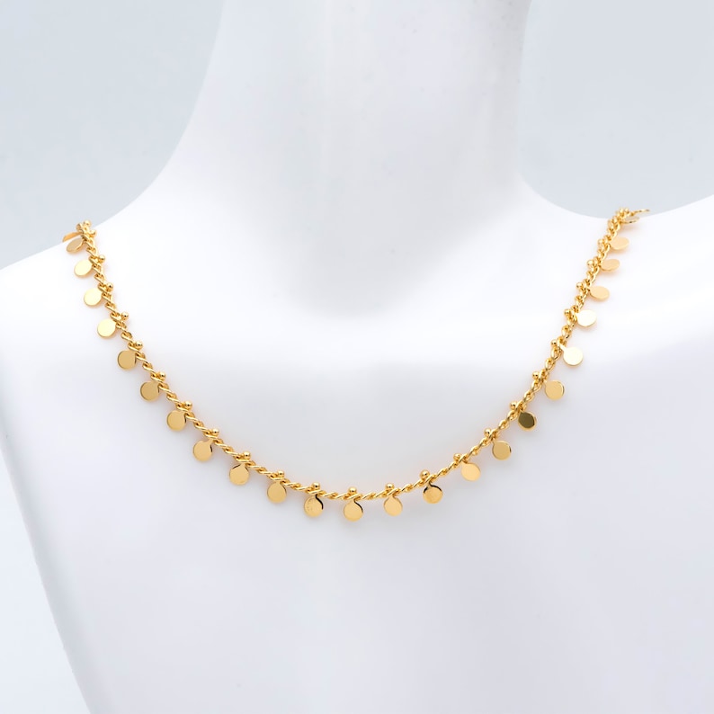 May include: A gold necklace featuring a fine chain with small round charms dangling from it.
