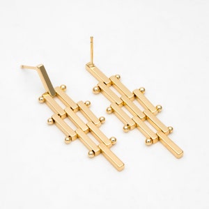 Puede incluir: Un par de pendientes geom&eacute;tricos de color dorado con un dise&ntilde;o largo y rectangular. Los pendientes est&aacute;n hechos de m&uacute;ltiples barras conectadas con peque&ntilde;as cuentas redondas en cada punto de conexi&oacute;n.