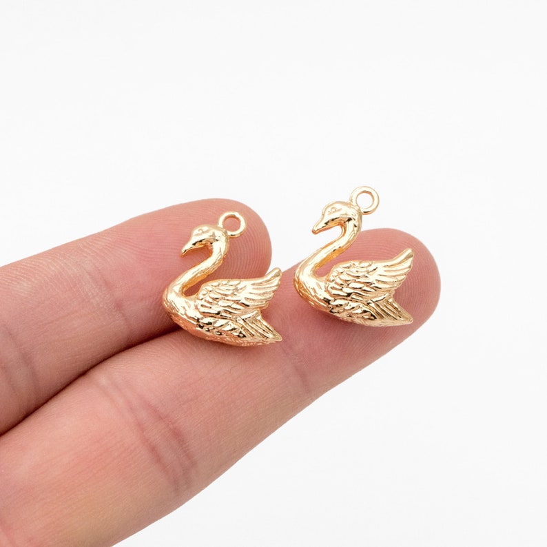 May include: Two gold-tone swan charms with a textured finish. The charms have a loop at the top for attaching to jewelry or other crafts.