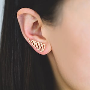 May include: A gold ear cuff in the shape of a continuous spiral, worn on the upper part of the ear.