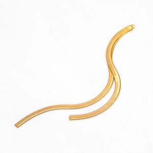 May include: A gold snake chain necklace. The chain is made of a series of small, interlocking links that create a smooth, flowing look.