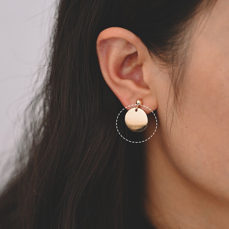 May include: Gold circle earrings with a smooth, shiny finish. The earrings are a simple and elegant design.