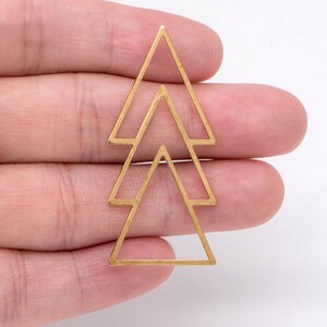 May include: A gold-colored metal pendant featuring a layered triangle design. The pendant consists of three nested triangles, each with a geometric, open-frame construction. The piece is likely intended for jewelry making or crafting.