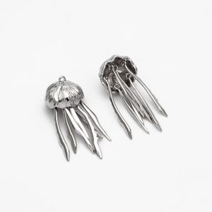 May include: Two silver-toned metal jellyfish charms with detailed tentacles. The charms are perfect for jewelry making or crafting projects.