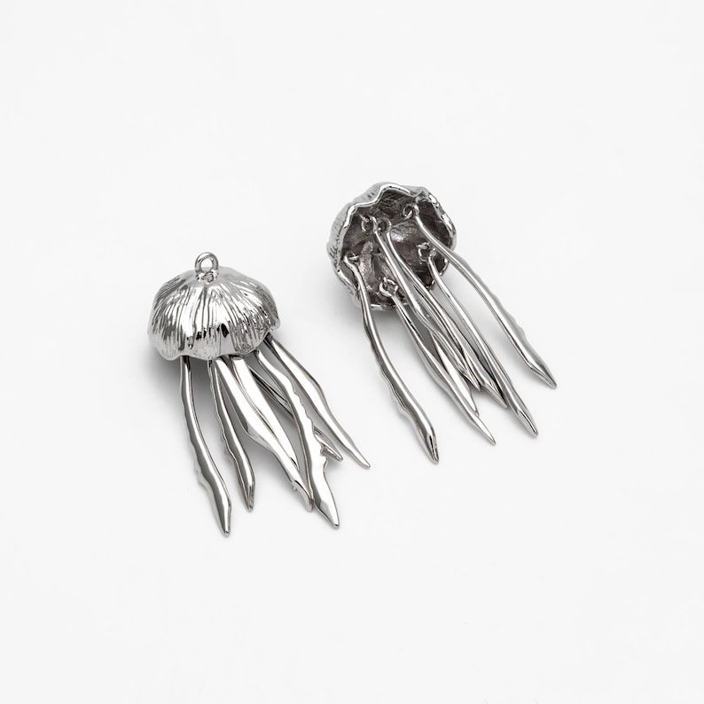 May include: Two silver-toned metal jellyfish charms with detailed tentacles. The charms are perfect for jewelry making or crafting projects.