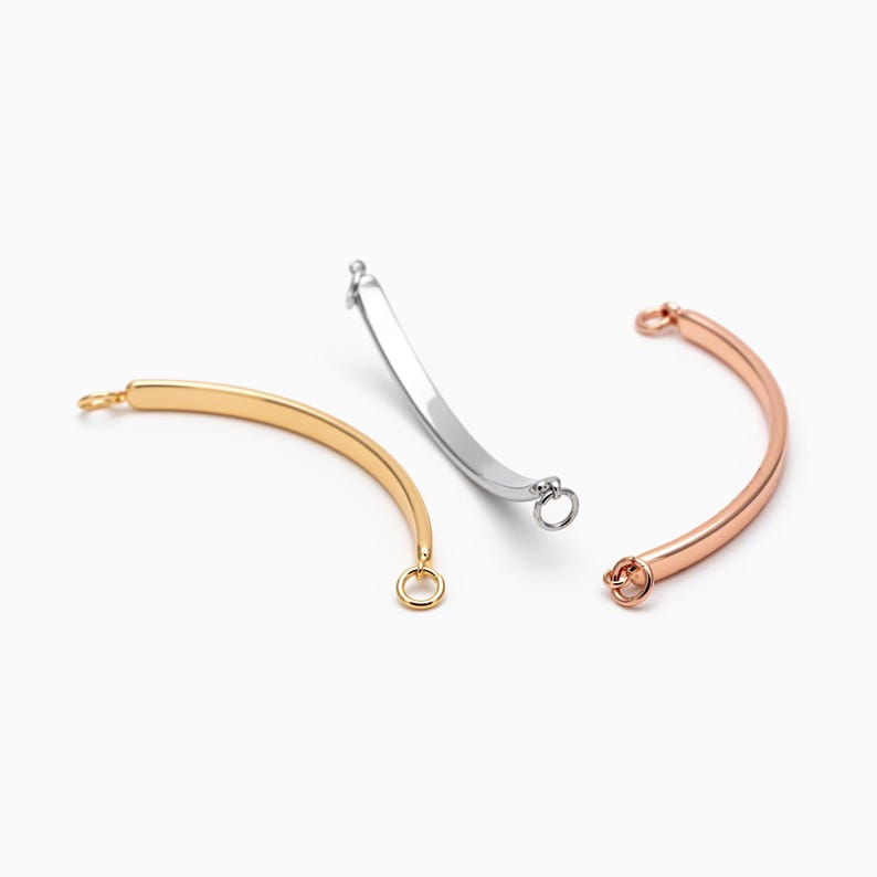 May include: Three metal bracelet extender clasps in silver, gold, and rose gold. Each clasp is a curved bar with a small ring at each end.