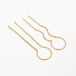 Op de afbeelding: Een set van drie gouden kettingoorbellen met een eenvoudig cirkelontwerp. Elke oorbel heeft een dunne gouden staaf met een ketting die aan een kleine gouden cirkel is bevestigd.