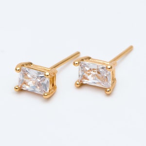 May include: A pair of gold earrings with clear rectangular stones. The earrings have a simple design and are perfect for everyday wear.