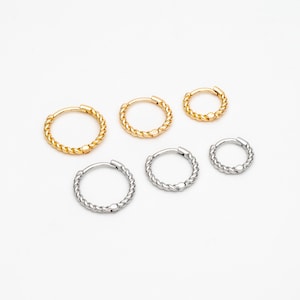 May include: Set of six gold and silver hoop earrings with a twisted rope design. The earrings are different sizes.