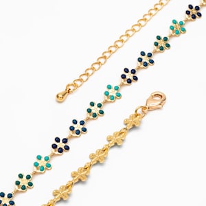 May include: A gold chain bracelet with a delicate flower design. The flowers are blue, green, and turquoise.