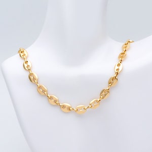 May include: A gold-colored necklace with a chain of flat, oval-shaped links. The necklace is displayed on a white mannequin bust. The links are evenly spaced and create a continuous, elegant design. The necklace has a bright, polished finish.