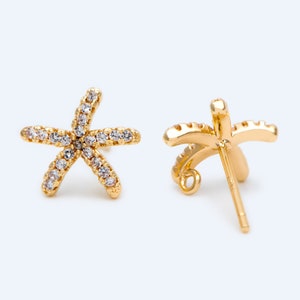 Puede incluir: Un par de pendientes de estrella de mar de tono dorado con piedras de circonita cúbica transparentes. Los pendientes se muestran desde el frente y la parte posterior.