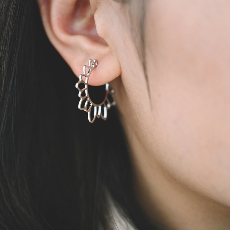 Puede incluir: Pendientes de aro de plata con un delicado dise&ntilde;o de sol. Los pendientes est&aacute;n hechos de un metal fino y tienen una forma ligeramente redondeada.
