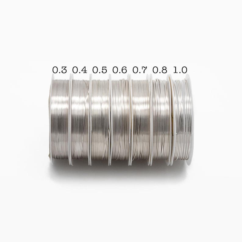 May include: A set of seven spools of silver wire, each labeled with a different gauge: 0.3, 0.4, 0.5, 0.6, 0.7, 0.8, and 1.0.