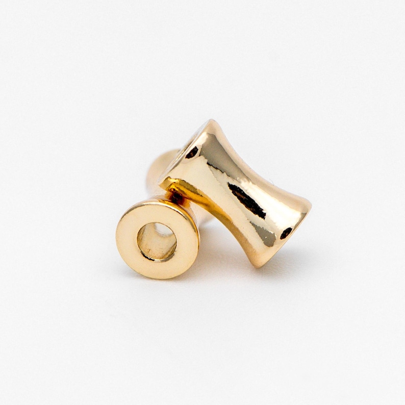 May include: Two gold-colored ear gauges, one is a flared cylinder and the other is a flat disc with a hole in the center.