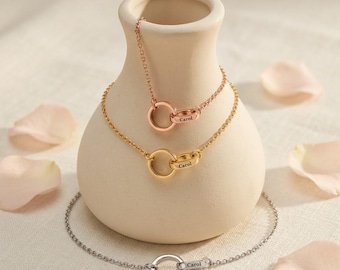 May include: Three delicate metal chain bracelets, each featuring a circular pendant engraved with the name Carol. The collection includes one rose gold, one yellow gold, and one silver-toned bracelet, all displayed on a smooth, light-colored vase.