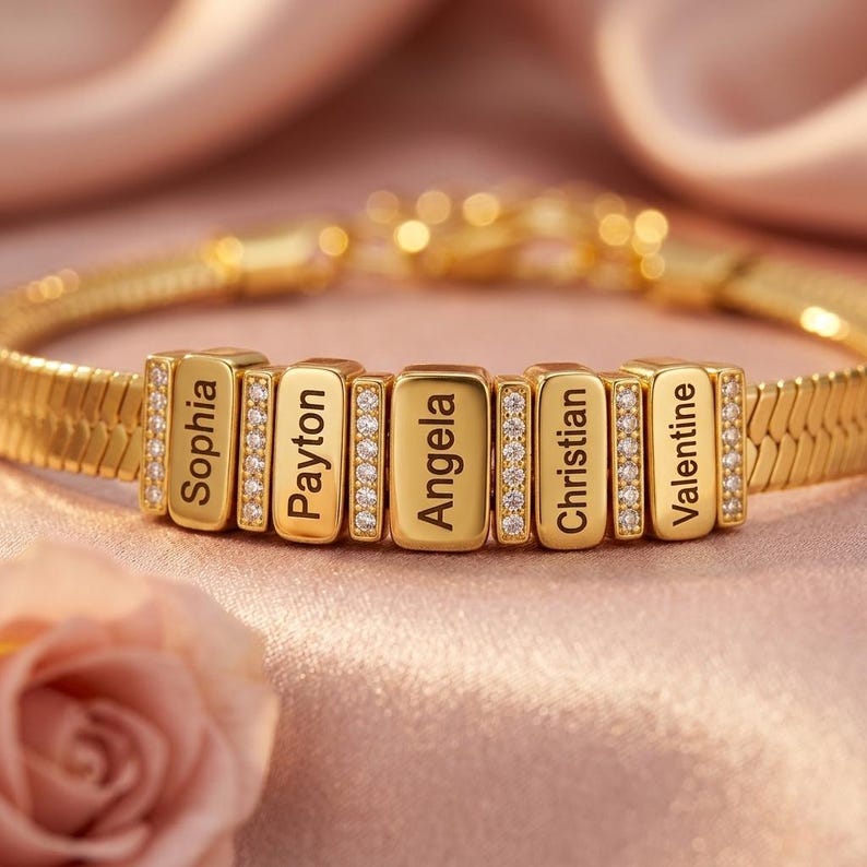May include: A gold-toned herringbone chain bracelet featuring five rectangular charms engraved with the names Sophia, Payton, Angela, Christian, and Valentine, interspersed with four vertical bars encrusted with small clear stones.