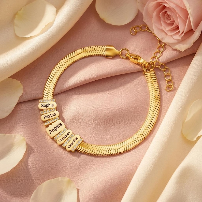 May include: A gold-toned herringbone chain bracelet featuring five rectangular charms, each engraved with a name: Sophia, Payton, Angela, Christian, and Valentine. The charms are accented with small clear stones and include a lobster clasp closure.