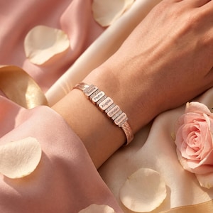 May include: A rose gold-toned bracelet featuring a flexible herringbone chain and five rectangular links. Each link is engraved with a name: Sophia, Payton, Angela, Christian, and Valentine. Small clear stones are set between each link.