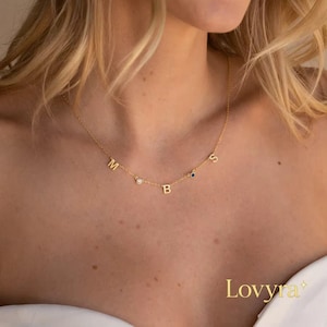 Peut inclure: Un délicat collier en or avec les lettres "M", "B" et "S" espacées le long de la chaîne. Le collier comporte de petites pierres précieuses entre les lettres. Le mot "Lovvra" est imprimé en bas à droite.