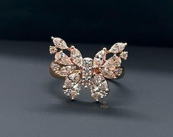 May include: A rose gold-toned ring featuring a butterfly-shaped centerpiece adorned with numerous marquise and round-cut clear stones. The ring displays the text MIKI in small letters at the base of the butterfly design, showcasing a detailed arrangement of sparkling stones.