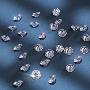 K&ouml;nnte beinhalten: Verstreute, klare Edelsteine ​​verschiedener Formen und Gr&ouml;&szlig;en, darunter runde und facettierte Schliffe, funkeln vor einem dunkelblauen Hintergrund. Die Edelsteine ​​reflektieren das Licht und erzeugen ein brillantes Funkeln. Das Bild zeigt eine Sammlung loser Diamanten.