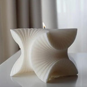 May include: A white, geometrically shaped candle with a flame burning at the top. The candle has a unique, folded design.