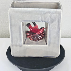 May include: A gray ceramic vase with a square opening featuring a red bird figurine inside. The vase has a textured, mottled glaze.