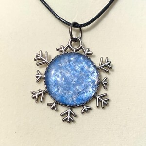 May include: A silver snowflake pendant necklace with a blue and white glitter resin snowflake charm.