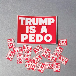 May include: A collection of red and white stickers with the text "TRUMP IS A PEDO". The stickers are in various sizes, with a large rectangular sticker and several smaller square stickers scattered around.