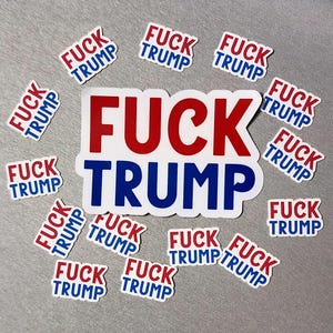 May include: A collection of stickers with the text "FUCK TRUMP" in red and blue, arranged on a gray surface. The stickers are white with the text in a bold, sans-serif font. The larger sticker has the same text.