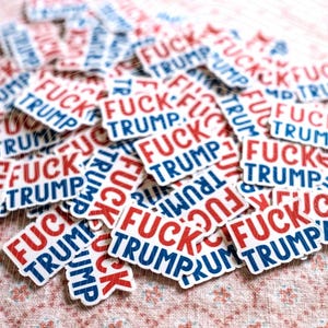 May include: A collection of small, rectangular stickers featuring the text FUCK TRUMP printed in a bold, sans-serif font. The word FUCK is displayed in red capital letters, while the word TRUMP is in blue capital letters on a white background.