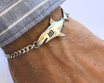 May include: A silver shark charm bracelet with a curb chain. The shark charm is detailed with gills and teeth.