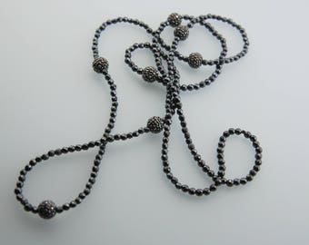 Pode incluir: Um colar de hematita preto com pequenas contas redondas facetadas e contas redondas facetadas maiores. O colar é em camadas e tem um comprimento longo.