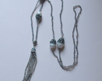 Pode incluir: Um colar longo de várias camadas com um tassel de contas cinzas. O colar apresenta pérolas brancas com detalhes pretos.