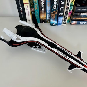 May include: A black, white, and red model spaceship with the word "TEMPEST" printed on the side. The model has a sleek design with wings and a long body. It is resting on a white surface.