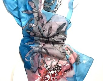 May include: A light blue silk scarf with a floral design. The flowers are pink, white, and gray with black outlines. The scarf is folded and draped over a white surface.